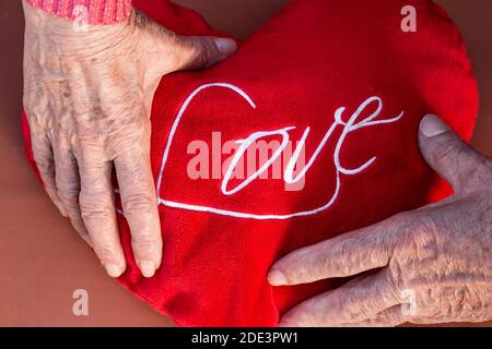 From above of crop anonymous romantic senior couple holding red heart with Love inscription Stock Photo