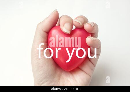 Woman hand hold red heart on the white background with text FOR YOU. Health insurance, donation, saving life concept