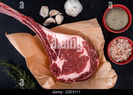 Freshly cut tomahawk ribeye steak with butcher's paper ready to be seasoned with salt and pepper, garlic and rosemary on a countertop Stock Photo