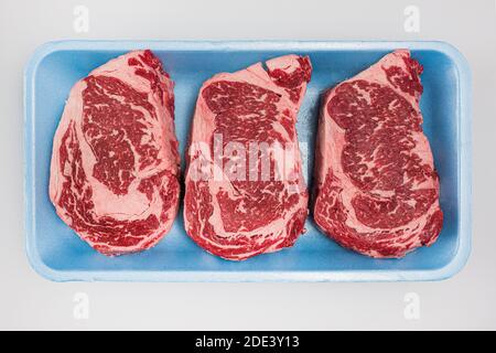 Three freshly cut prime grade boneless ribeye steaks being packaged on a butcher table Stock Photo