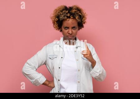 African woman pointing with finger up and angry expression, showing warning gesture. Studio shot on pink wall. Stock Photo