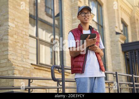 Tracking order. Young asian male courier using app on digital tablet while standing on the street. Delivery services concept Stock Photo