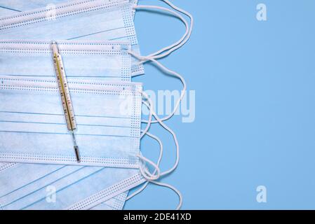 Medical surgical protective face masks and glass thermometer for measuring the temperature of the human body on light blue background. Stock Photo