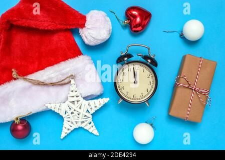 Santa Claus hat, alarm clock, gift box and decorative Christmas ornaments on blue background. The concept of celebrating the New Year and Christmas. Stock Photo