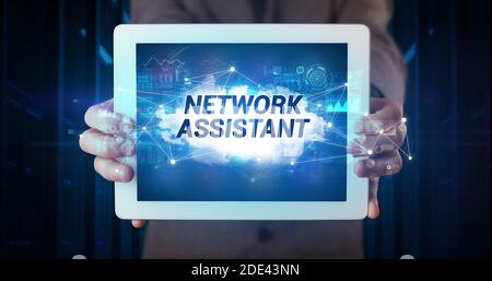 Young business person working on tablet and shows the inscription: NETWORK ASSISTANT Stock Photo