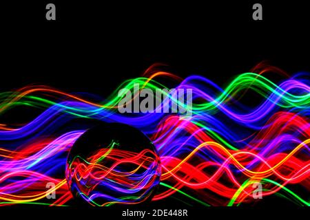 Long exposure photograph of neon multi colour in an abstract swirl pattern with reflective glass ball. Light painting photography. Stock Photo