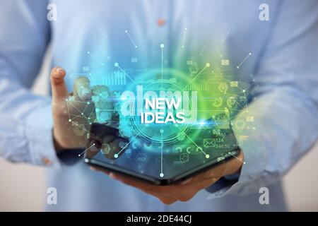 Businessman holding a foldable smartphone with NEW IDEAS inscription, new business concept