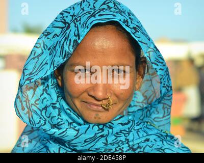Young Indian Rabari tribal woman from Kutch with precious nose jewelry and traditional face tattoo on chin poses in bright sunlight for the camera. Stock Photo