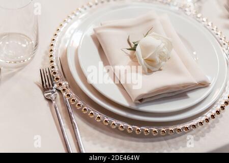 Set of plates and napkin with rose on the beige background. Luxury table set in the restaurant. Glasses and plates. Wedding banquet.  Stock Photo