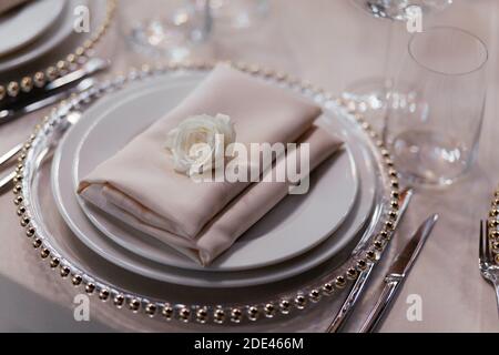 Set of plates with beige napkin above. Luxury table set in the restaurant. Glasses and plates. Decorations. Beige background. Wedding banquet.  Stock Photo