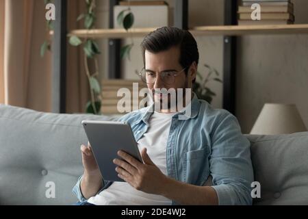 Caucasian man sit on couch using tablet gadget Stock Photo