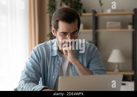 Pensive Caucasian man look at laptop screen thinking Stock Photo