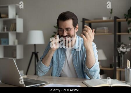 Happy man sit at desk talking on smartphone Stock Photo
