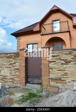 Modern brick house under construction with stone fence and metal entrance door. Stock Photo