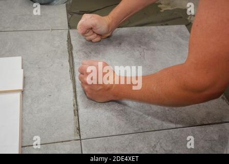 Worker installing ceramic tile on the floor, bathroom flooring Stock Photo