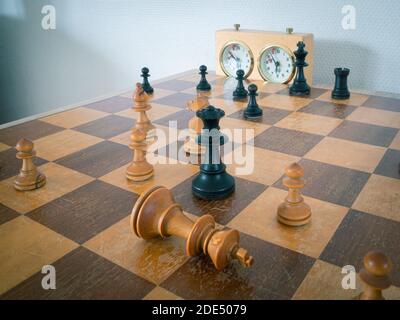White king and black queen in a game of chess. White has resigned and placed his king flat on the chessboard. Stock Photo