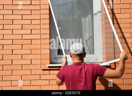 Man installing mosquito net, mosquito wire screen on brick house window Stock Photo