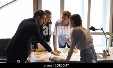 Diverse teammates standing around work table applying corrections to project Stock Photo