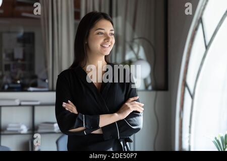 Happy young indian lady standing by window in good mood Stock Photo