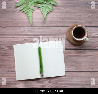 Open notepad with pen, coffee and green plants on wood table. Top view. Stock Photo