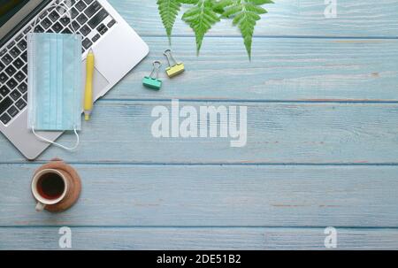 Wood table with computer laptop, face mask, coffee, supplies and green plants. Stock Photo