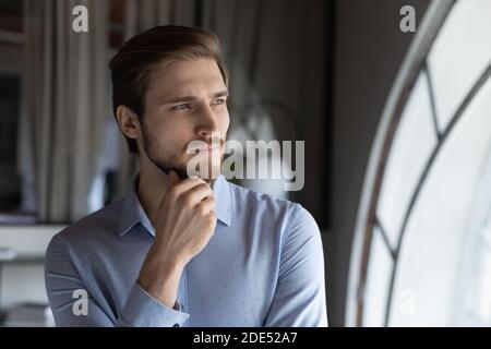 Thoughtful young man leader looking at window visualizing business opportunities Stock Photo