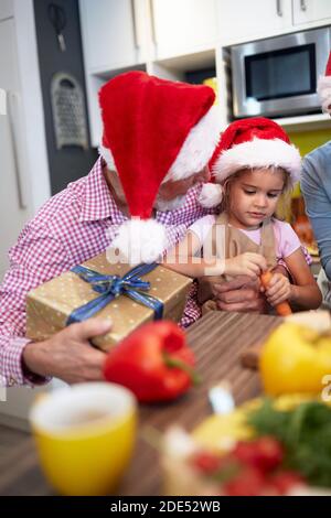 Grandpa in the kitchen in festive atmosphere having a Xmas present for granddaughter. Christmas, family, together Stock Photo