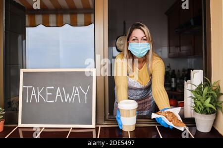 Young woman wearing face mask while serving takeaway breakfast and coffee inside bakery cafe Stock Photo