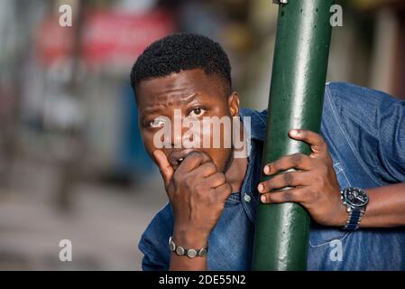 young african man behind iron bar looking at the camera, surprised. Stock Photo