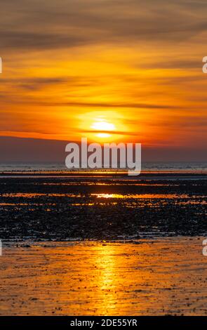 Low sun going down behind clouds on a beautiful evening at the seaside, at low tide. Sunset in Winter in the UK. Portrait. Stock Photo