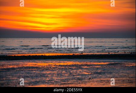 Orange red sky just after sunset at the coast, showing sun reflecting in the sea in the UK. Stock Photo