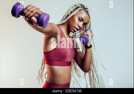 Close up portrait of female athlete working out using dumbbells. Fit woman with long braided hair training with dumbbells. Stock Photo