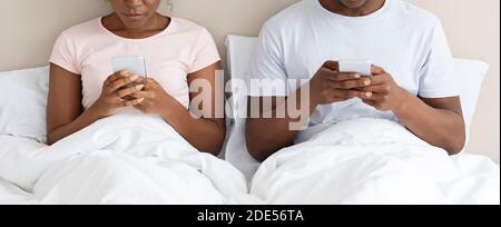 Unrecognizable black couple using smartphones in bed Stock Photo