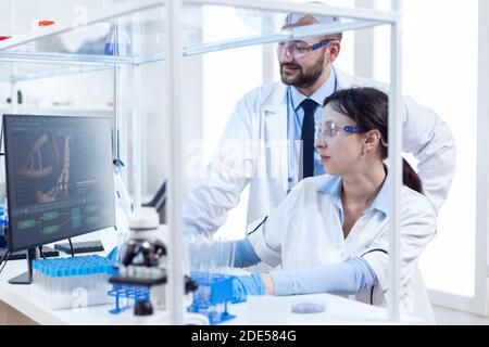 Two scientists are working together in laboratory using computer at workplace. Team of researchers doing pharmacology engineering in sterile lab for healthcare industry. Stock Photo