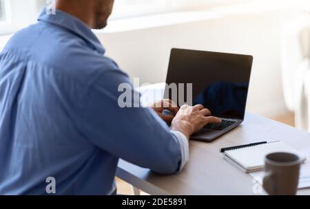 Unrecognizable businessman working on laptop with black screen in office, mockup image Stock Photo