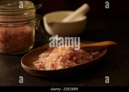 Himalayan pink salt crystals in a wooden dish, with a mortar and pestle and glass storage jar , England, Uk, Gb. Stock Photo