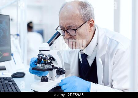 Senior scientist working on busy laboratory using modern microscope with slides. Chemist researcher in sterile lab doing experiments for medical industry using modern technology. Stock Photo