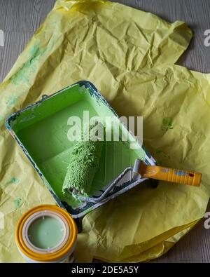 Paint roller in paint tray with green color in the tray on yellow paper. Stock Photo