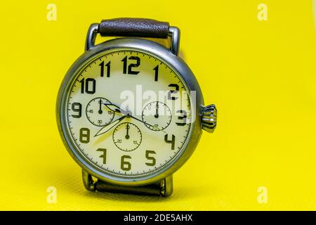 Rustic wristwatch with large watch face and leather stapes. Casual, fashionable and vintage brown male watch on yellow isolated background. Copy text Stock Photo