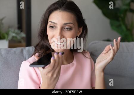 Smiling pretty millennial arabic indian woman recording audio message. Stock Photo