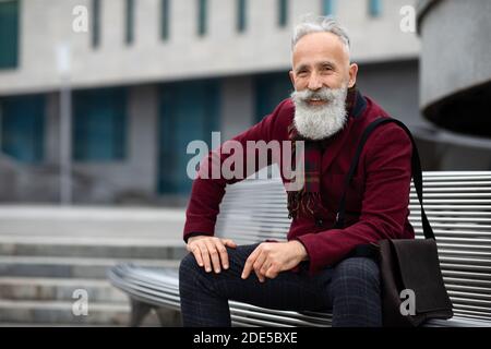 Handsome aged man sitting on bench, smiling at camera Stock Photo