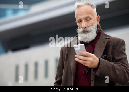 Grey-haired businessman using smartphone on the street Stock Photo