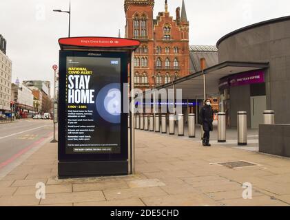 A man wearing a protective face mask walks past a Stay Home sign on a bus stop in King's Cross during the second national lockdown in England. London, United Kingdom 21 November 2020. Stock Photo