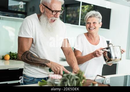 Crazy senior couple cooking together at home - Joyful elderly lifestyle and food nutrition concept - Main focus on woman face Stock Photo