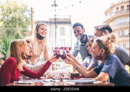 People toasting wine at restaurant bar with open face mask - New normal lifestyle concept with happy friends having fun together - Selective focus on Stock Photo