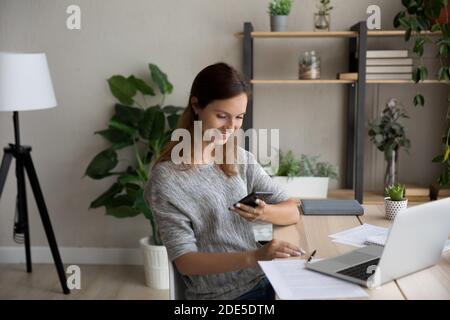Distracted from online computer work young woman using smartphone. Stock Photo