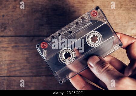 Hand holding audio cassette tape on brown old wooden table. Minimalism retro style concept. Background pattern for design. Stock Photo