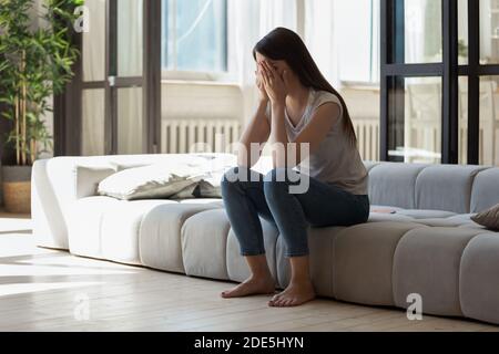 Unhappy young woman covering face with hands, crying alone Stock Photo