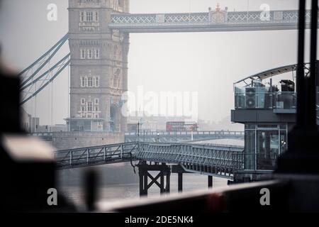 Red London Bus driving over Tower Bridge and River Thames in foggy misty weather in London City Centre on Coronavirus Covid-19 lockdown day one, England, UK