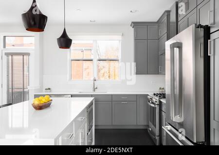 A modern kitchen with grey cabinets, a bowl of lemons on the white granite counter tops, and dark hardwood floors. Stock Photo